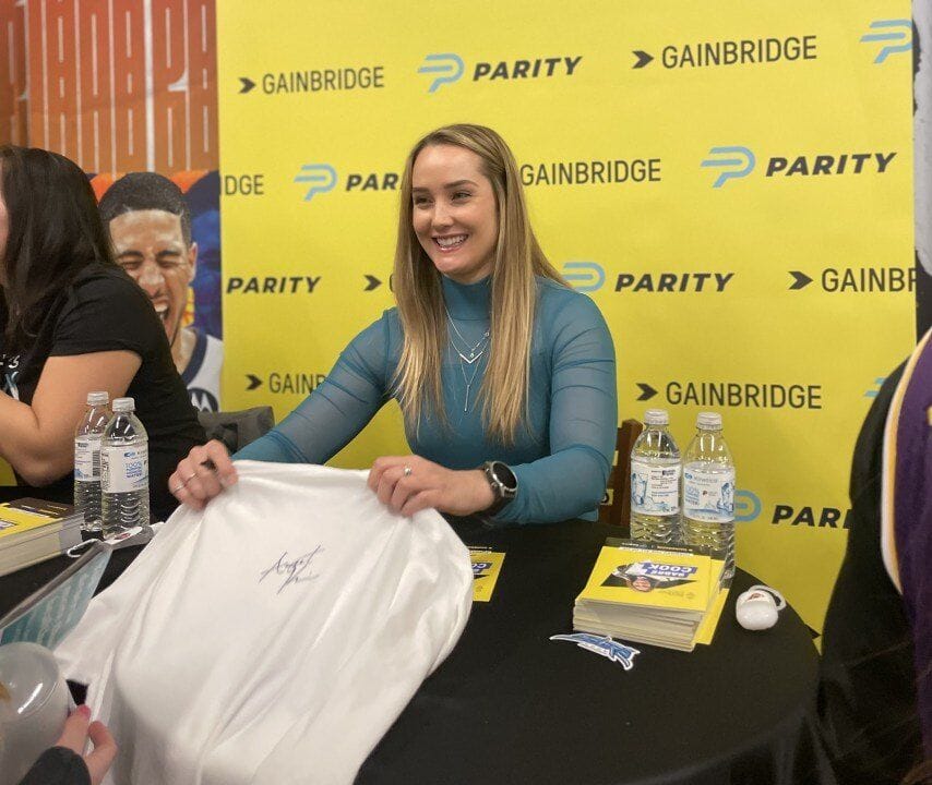 Parity athlete sitting at a table signing memorabilia for fans