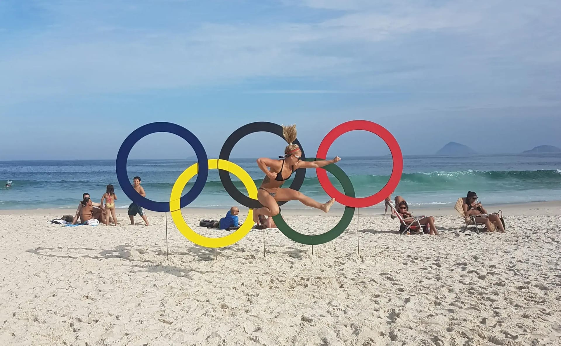 Morghan King leaps in the air in front of Olympic rings on a beach