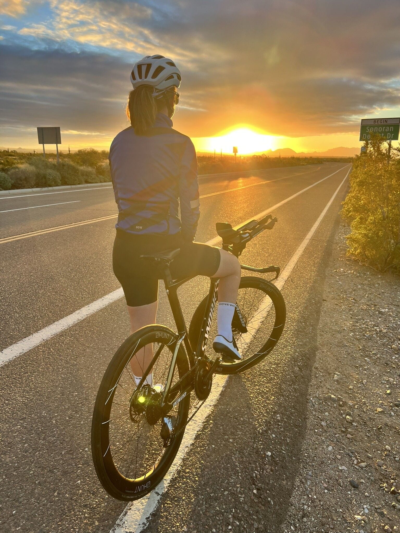 Samantha stands roadside with her bike watching the sunset