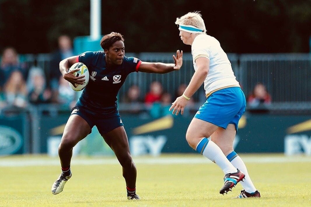 Naya holding the ball and blocking an opponent at a rugby game