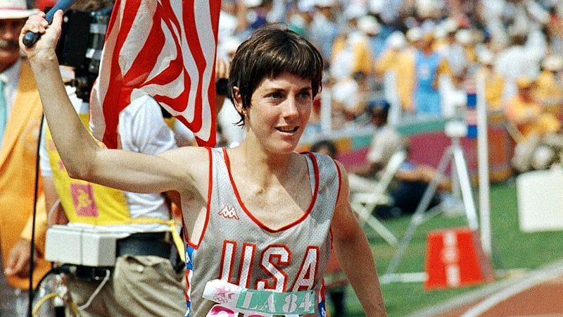 Joan Benoit carries a US flag on the Olympic track